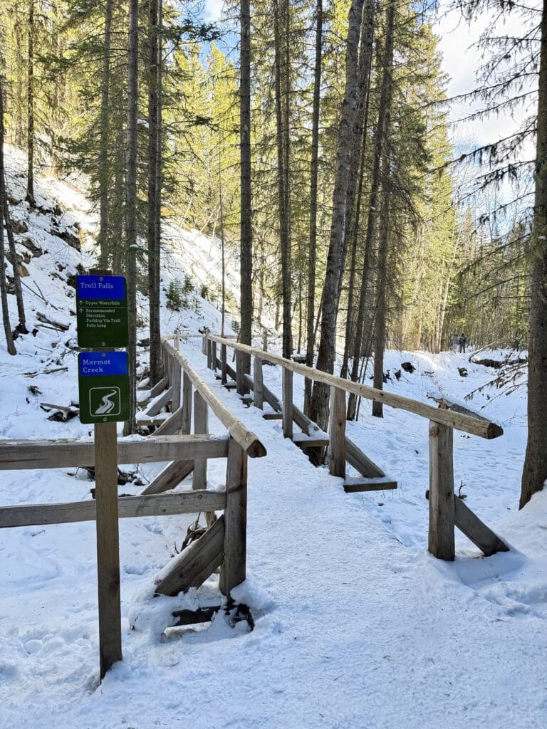 A small wooden bridge on a frozen creek connecting Troll Falls Kananaskis and the path to Upper Falls