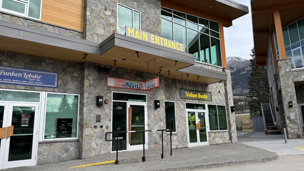 Front entrance of Canmore Downtown Hostel with stone facade, located near restaurants and shops in the heart of Canmore with mountain views in the background