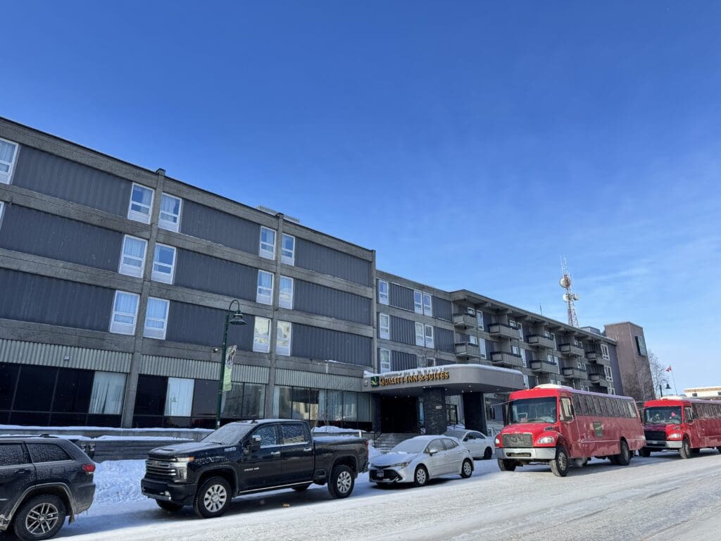 Four-storey hotel in Yellowknife with many cars and tour buses at the front door