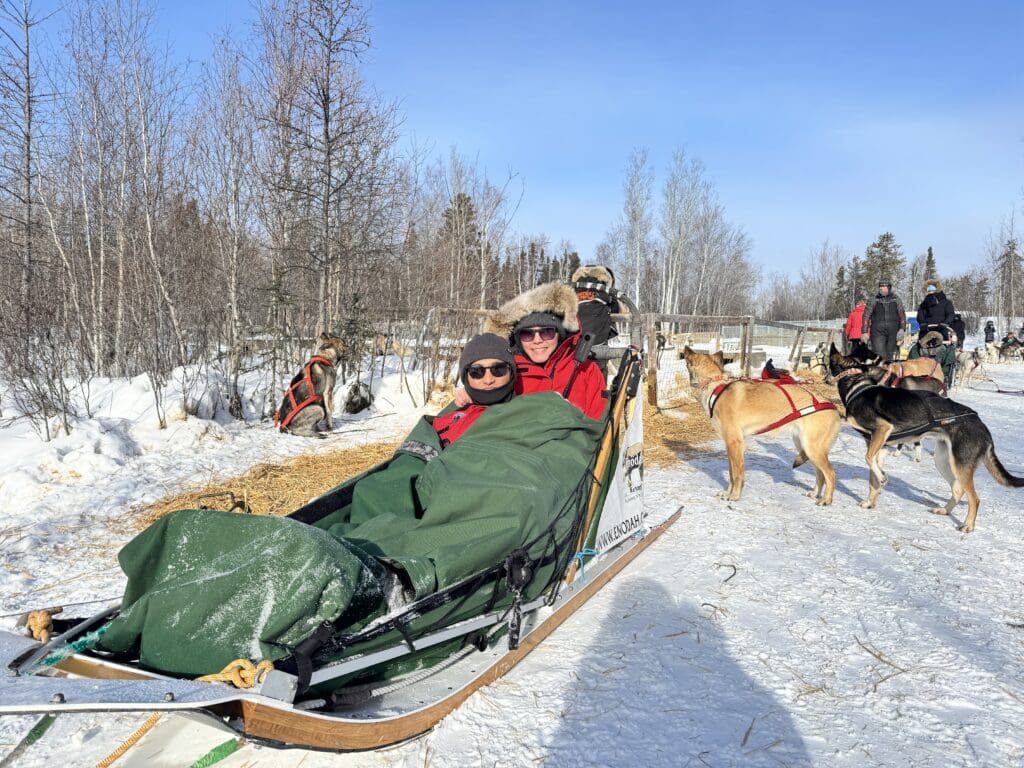 Sitting in sled with extra layer to protect us from wind when waiting for dog sledding in Yellowknife. Extreme cold weather gear.