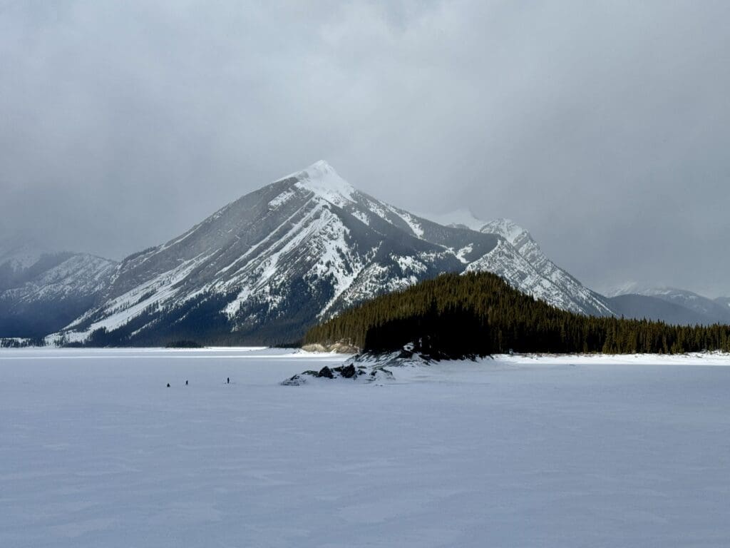Some people is standing far away in the middle of the snow-covered Kananaskis Lake