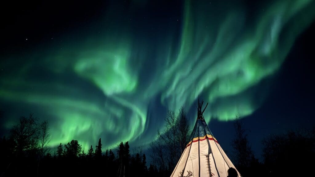 Spectacular aurora on the lounge of our aurora tour with a decorative indigenous camp in Yellowknife