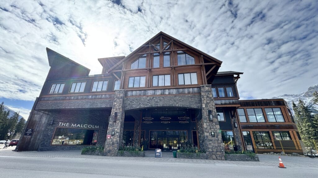 Front view of The Malcolm Hotel in Canmore, Alberta, featuring rustic alpine architecture with timber and stone design set against the backdrop of the Canadian Rockies