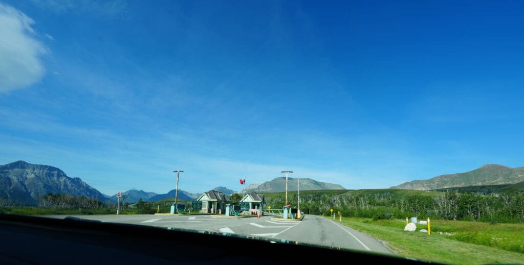 A road leads to a park gate in Waterton Lakes National Park, Alberta under a clear blue sky. Mountains form the backdrop, creating a serene and expansive landscape.
