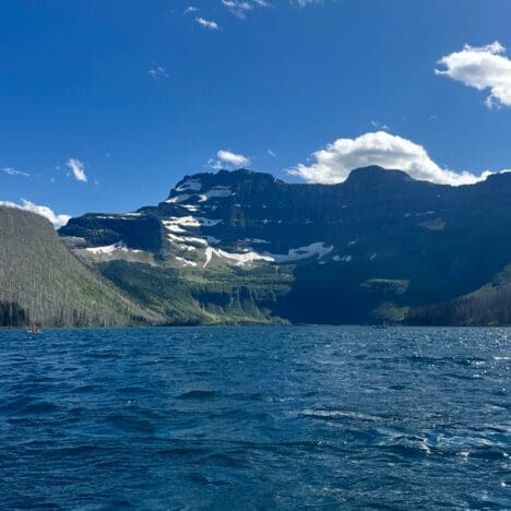 A serene mountain Cameron Lake in Waterton Lakes National Park, Alberta with rippling blue water under a clear sky. Snow-capped peaks rise in the background, evoking tranquility and grandeur.