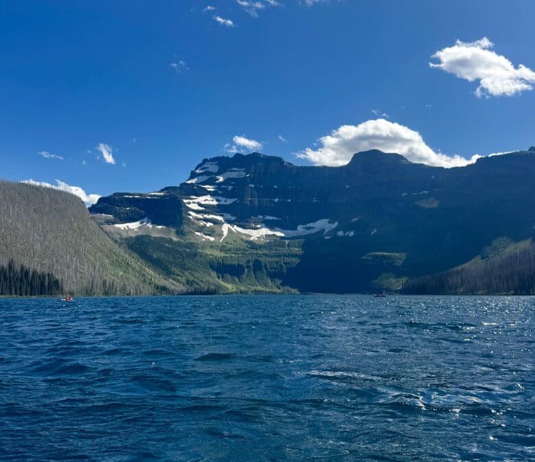 A serene mountain Cameron Lake in Waterton Lakes National Park, Alberta with rippling blue water under a clear sky. Snow-capped peaks rise in the background, evoking tranquility and grandeur.